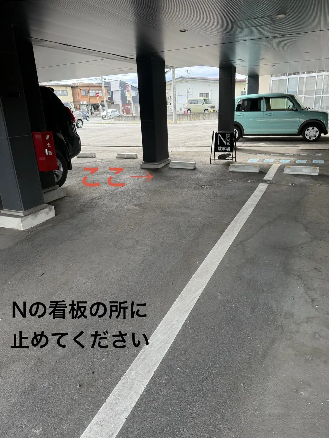 建物の駐車場内、「N eutral 駐車場」の看板の手前にある専用駐車スペース。写真には「ここ→」「Nの看板の所に止めてください」と書かれている